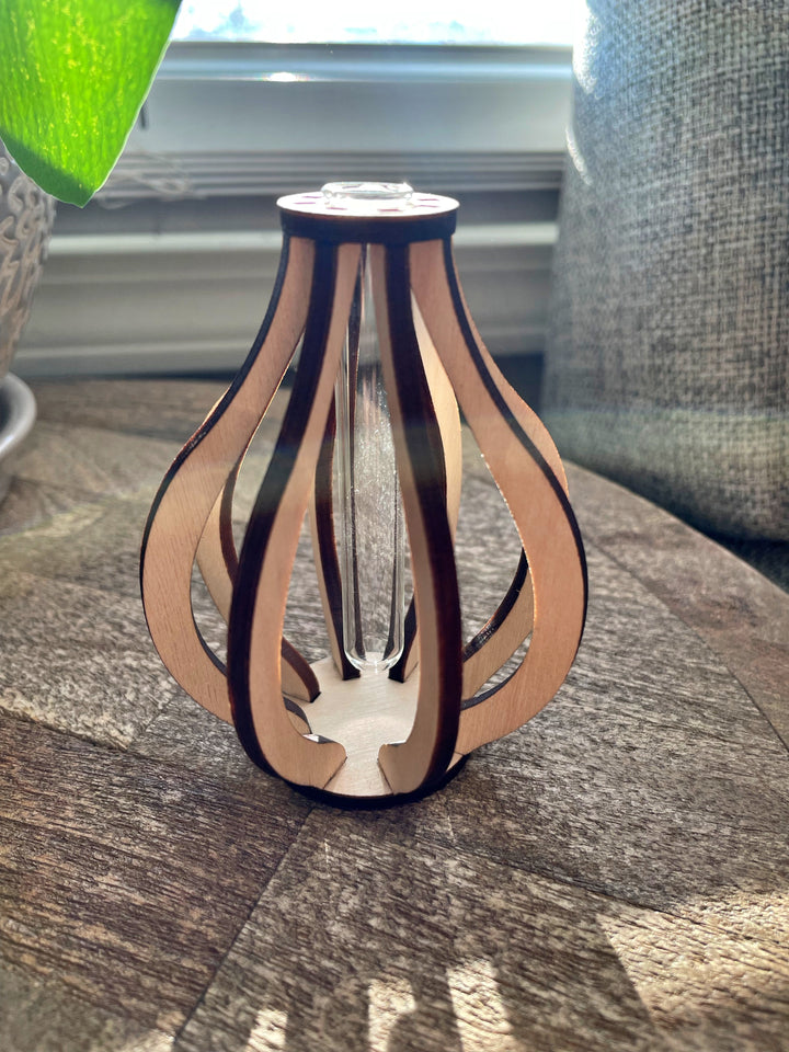 This small wooden bud vase is made from ten pieces of precision cut Baltic birch. At its center is a glass test tube to hold a fresh flower stem, cutting for propagation, or a dried floral bud.  SIZE: 3.5" tall 2.75" wide Mini test tube: 0.4" diameter   *DOES NOT INCLUDE PLANT Explore the best and coolest gift ideas for plant enthusiasts! Terra Cotta Plant Boutique serves the Toledo, Ohio area. Our online retail store ships nationally!